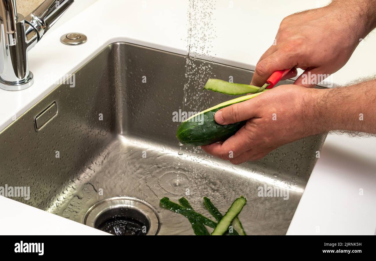 Il cetriolo nelle mani maschili è sbucciato per mangiare Foto Stock