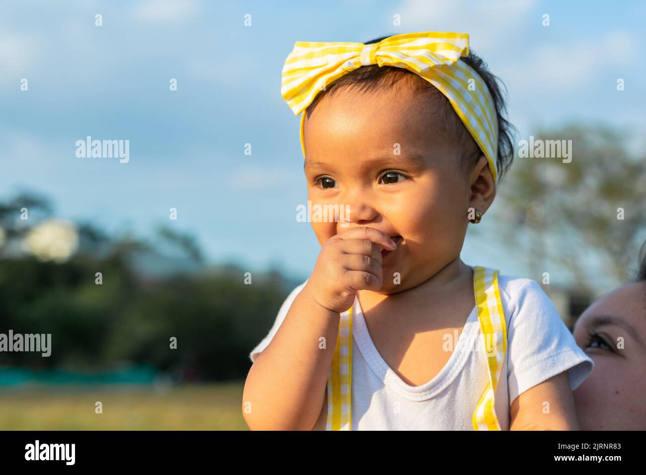 primo piano di una bella bambina di latina con una mano sulla bocca sorridente in un campo all'aperto in una bella giornata estiva. Foto Stock
