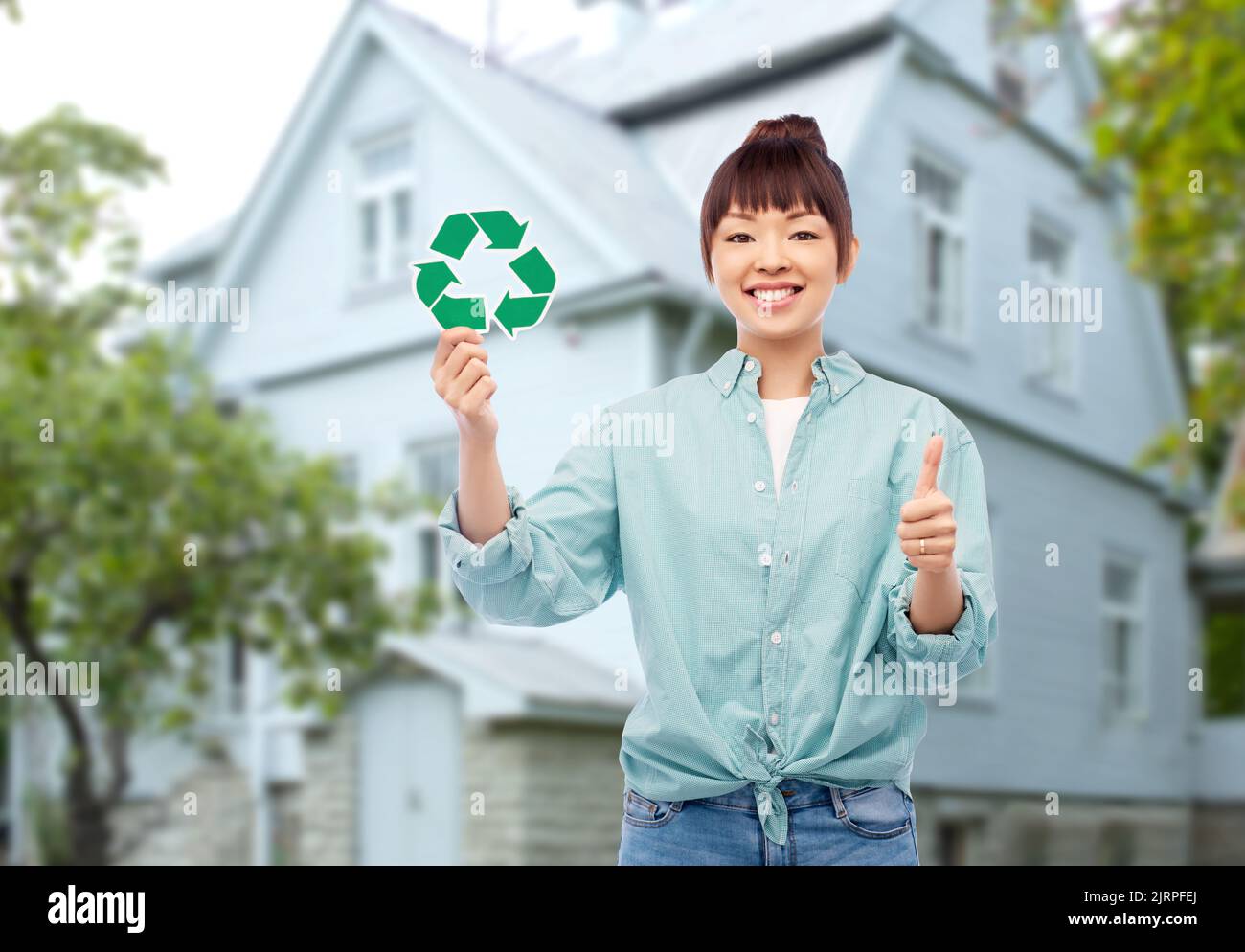 donna asiatica sorridente con un cartello verde di riciclaggio Foto Stock