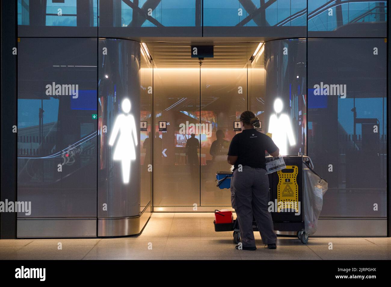 Una donna di pulizia si prepara ad entrare e pulire le donne loos (a sinistra) e maschio toilette / toilette / toilette / ingresso porta (a piedi senza porta) aeroporto di Ginevra, Svizzera (131) Foto Stock