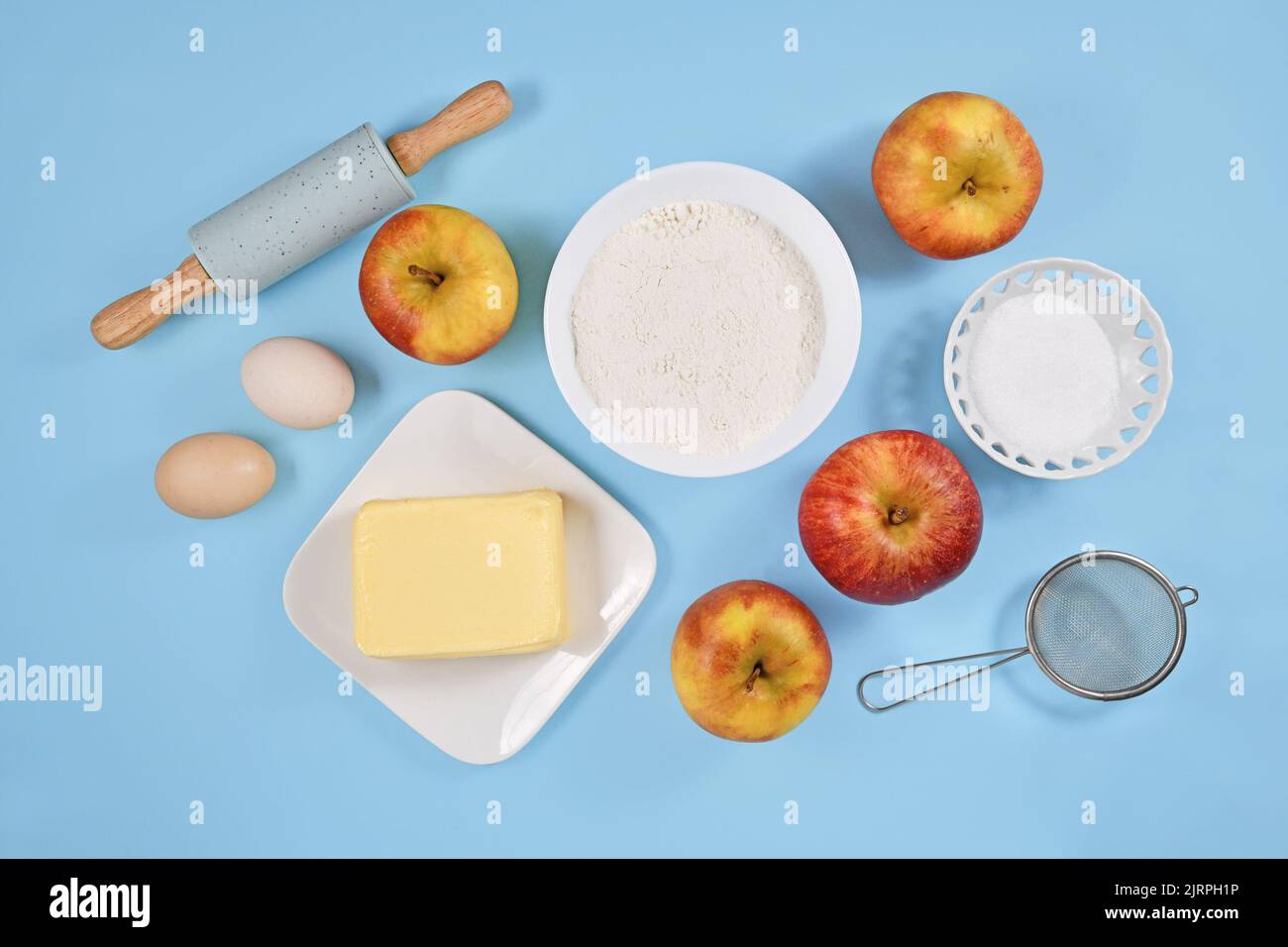 Ingredienti per la cottura della torta di mele con burro, farina, zucchero, uova e frutta su sfondo blu Foto Stock