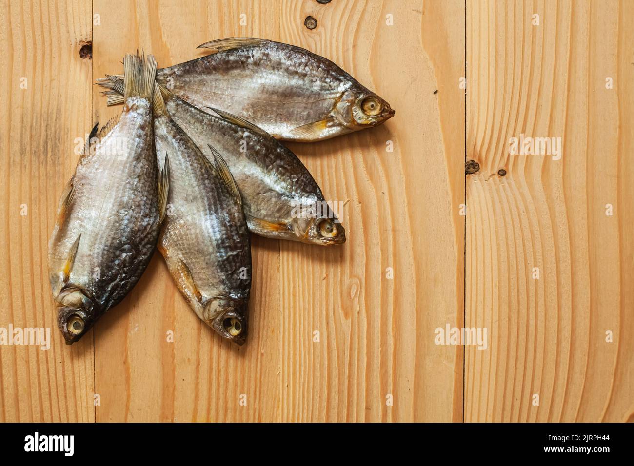 Pesce affumicato essiccato, su un asse di legno chiaro, vista dall'alto. Quattro pesci secchi su uno sfondo di legno. Foto Stock