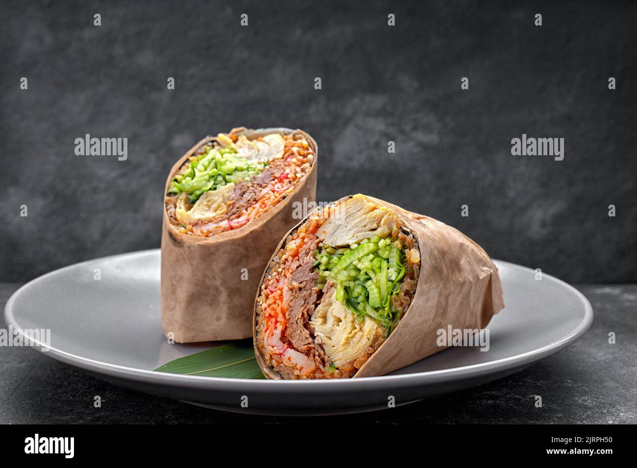 Sushi roll con tacchino e uova strapazzate, temaki, su un piatto, su cemento grigio Foto Stock