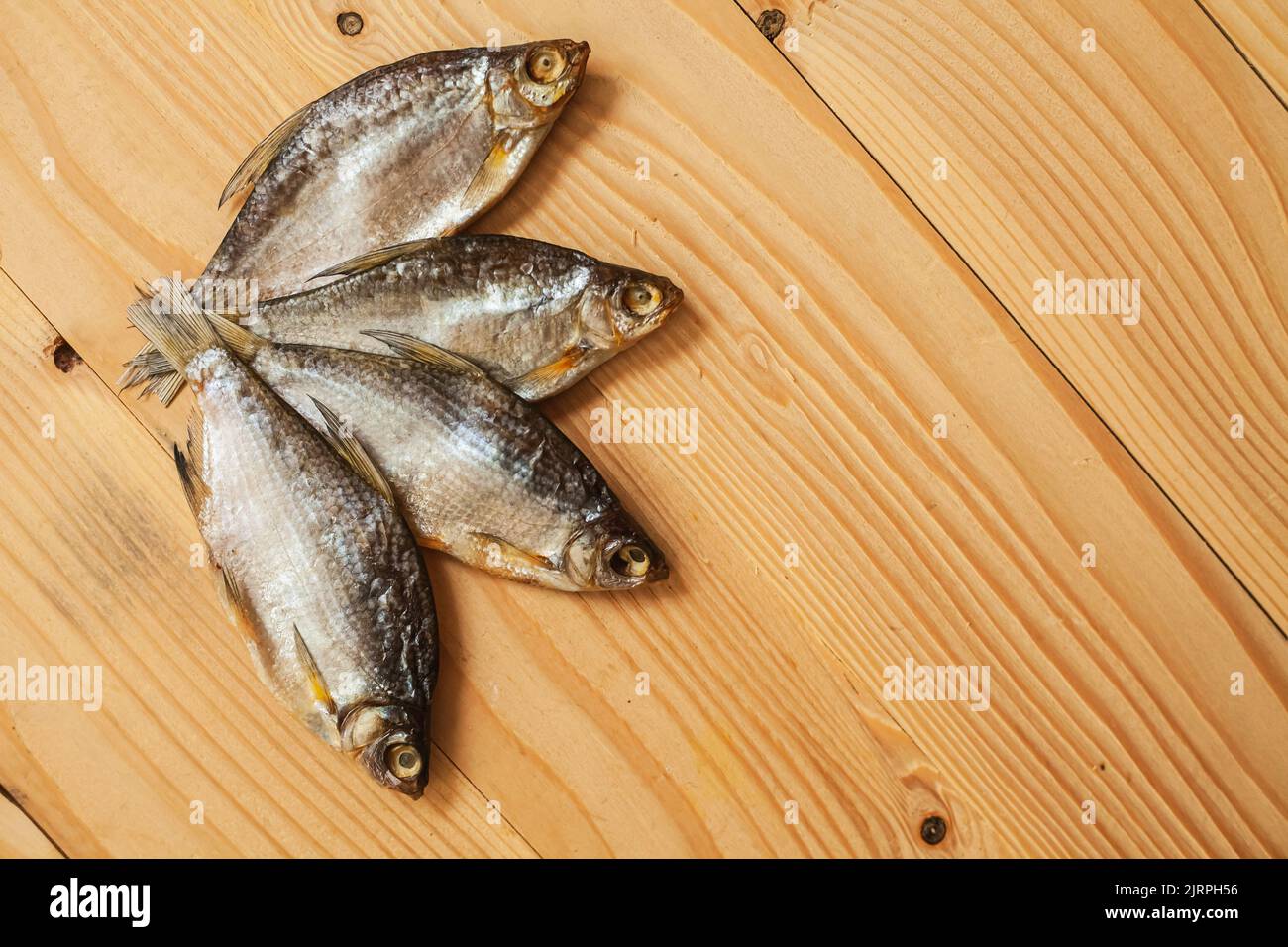 Pesce affumicato essiccato, su un asse di legno chiaro, vista dall'alto. Quattro pesci secchi su uno sfondo di legno. Foto Stock
