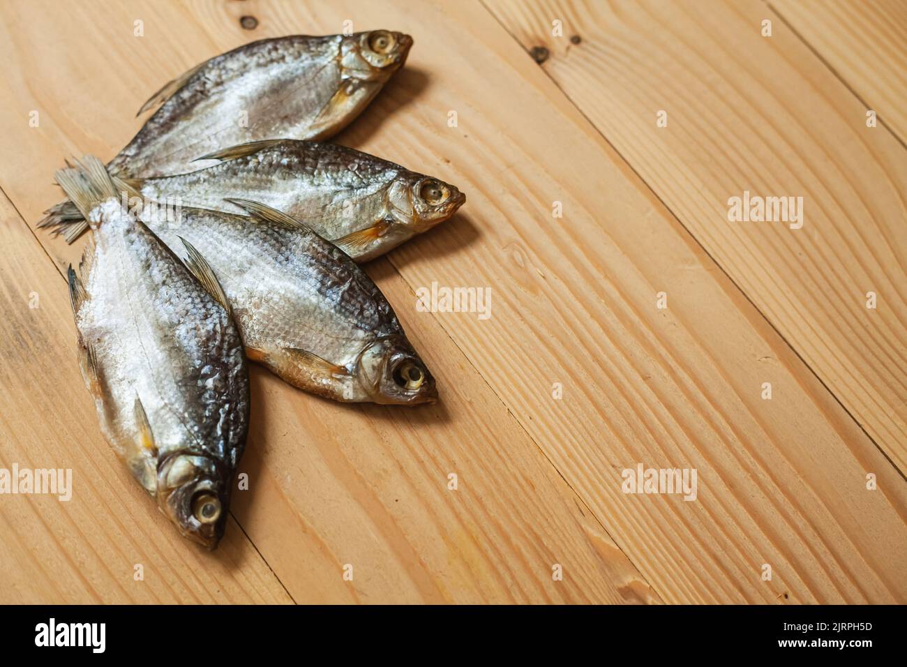 Pesce salato essiccato su uno sfondo di legno. Il pesce è completamente salato con la testa e visceri. Foto Stock