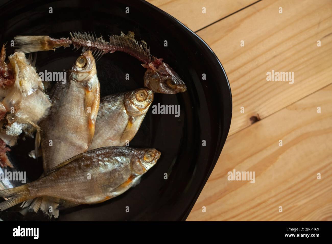 Pulito pesce secco, ossa e colonna vertebrale con testa in un piatto. Scheletro di pesce. Pesce salato essiccato su un piatto nero. Foto Stock
