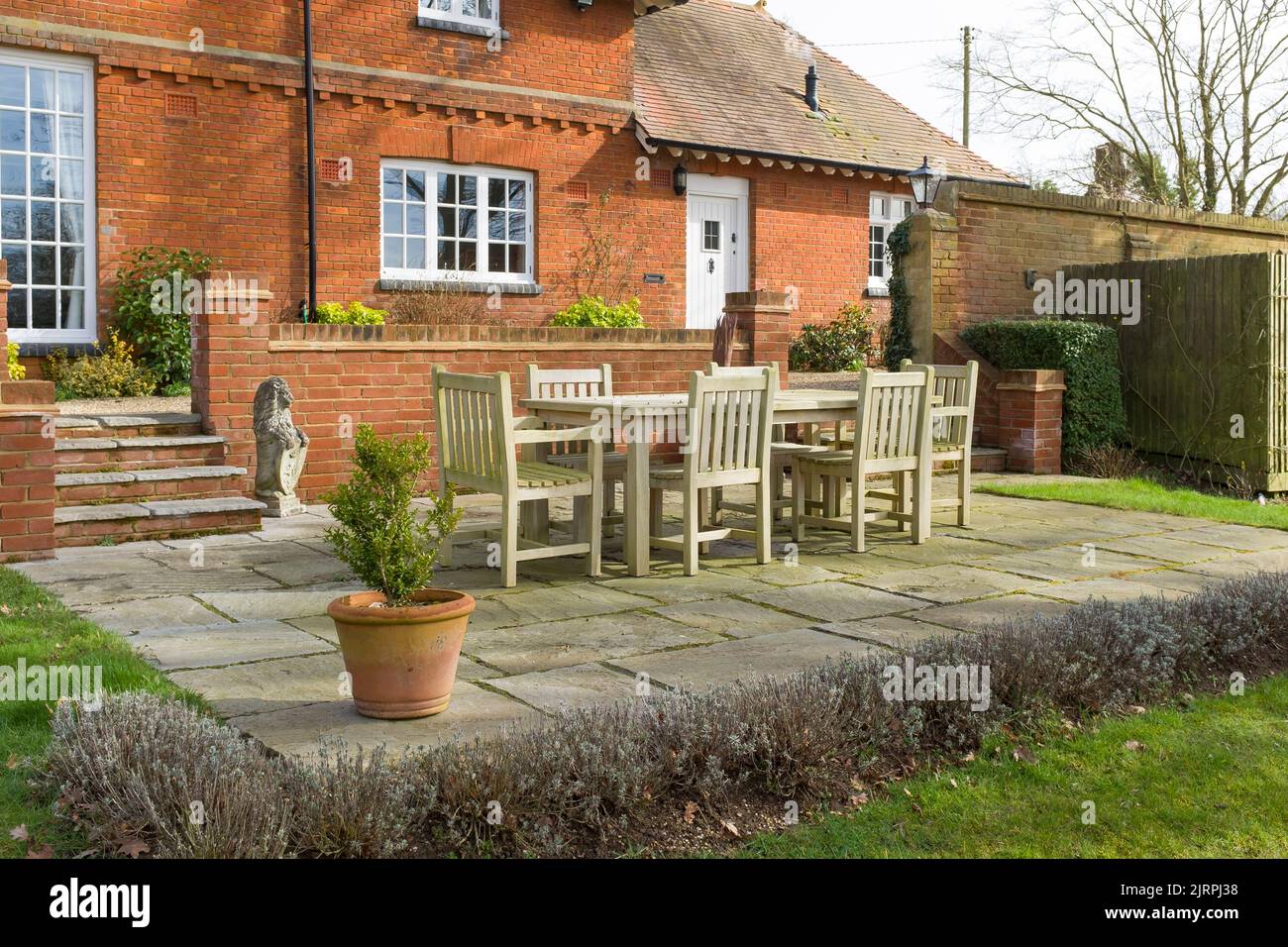 Giardino patio in inverno in un giardino all'inglese. Terrazza pavimentata con mobili in teak fuori di una vecchia casa di carattere, Regno Unito Foto Stock