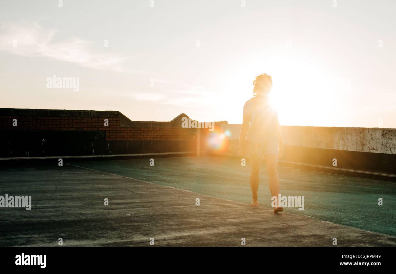 donna che cammina a piedi nudi con il suo skateboard al tramonto Foto Stock