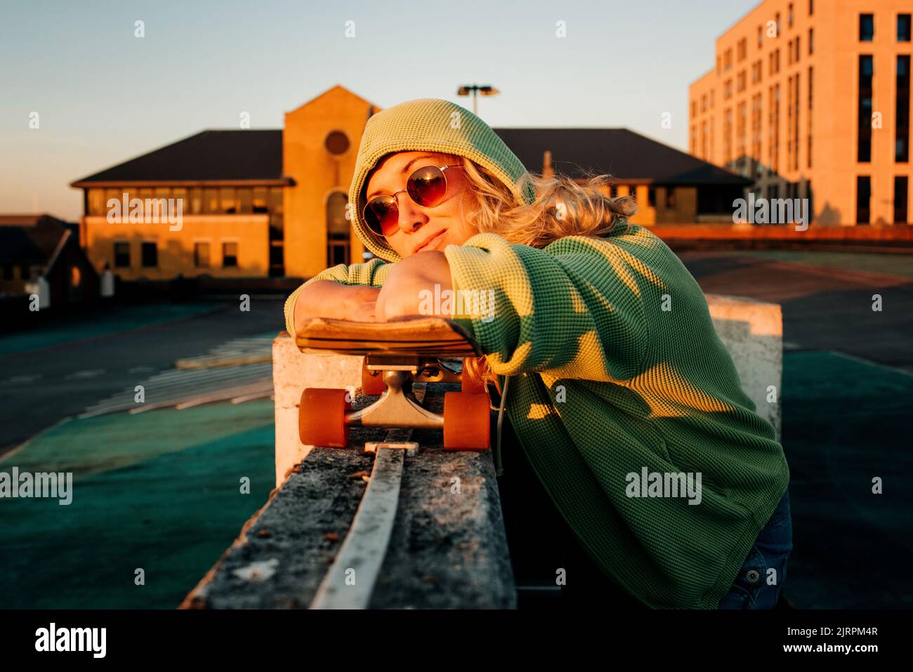 donna appoggiata sullo skateboard in un parcheggio al tramonto Foto Stock