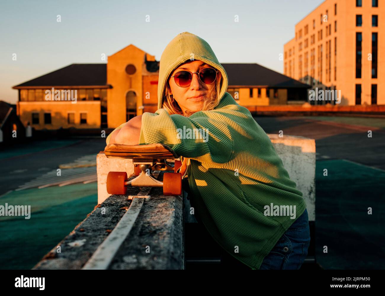 donna appoggiata sullo skateboard in un parcheggio al tramonto Foto Stock