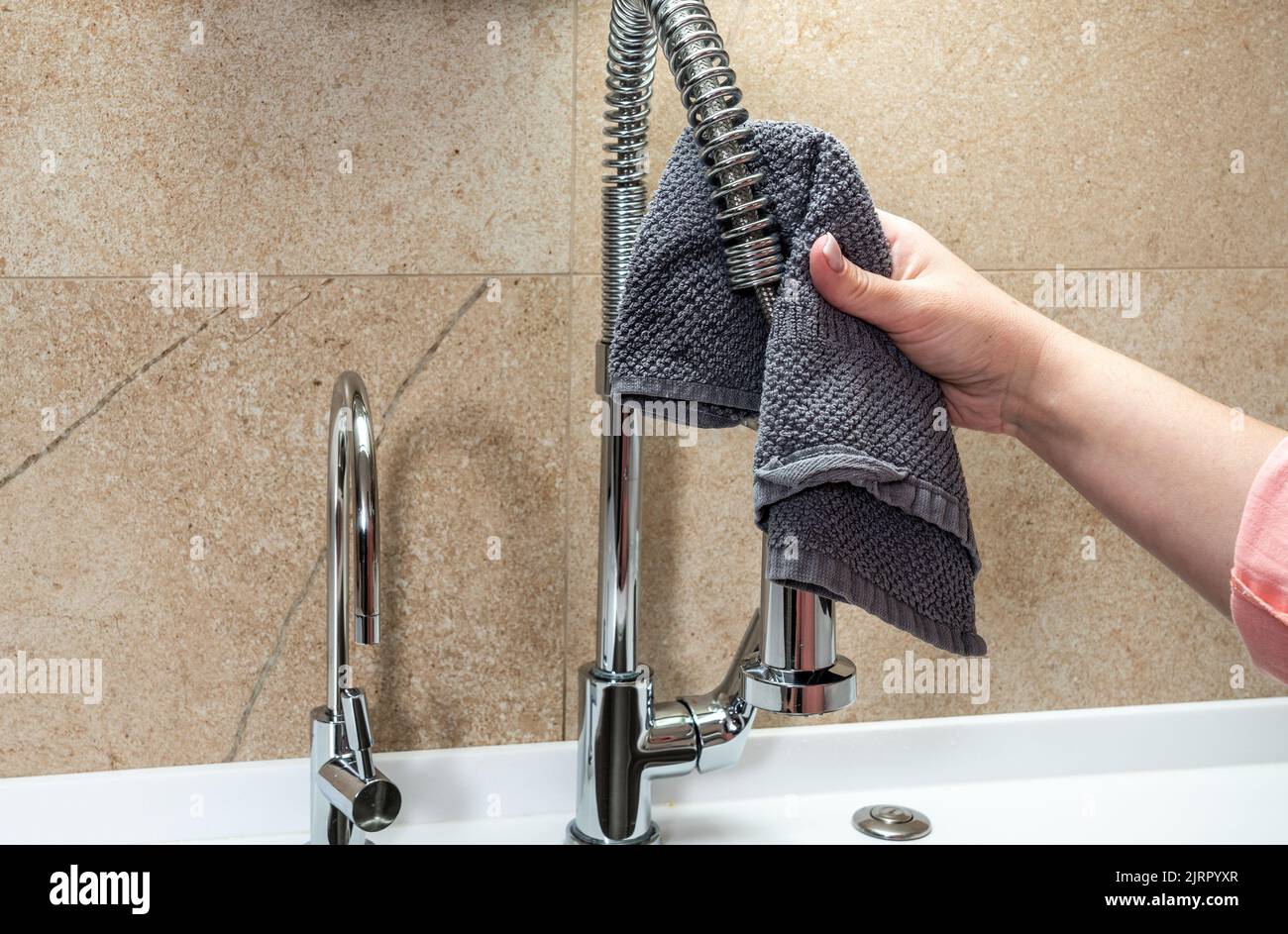 La mano di una donna sta strofinando un rubinetto da cucina sopra un lavandino con uno straccio Foto Stock