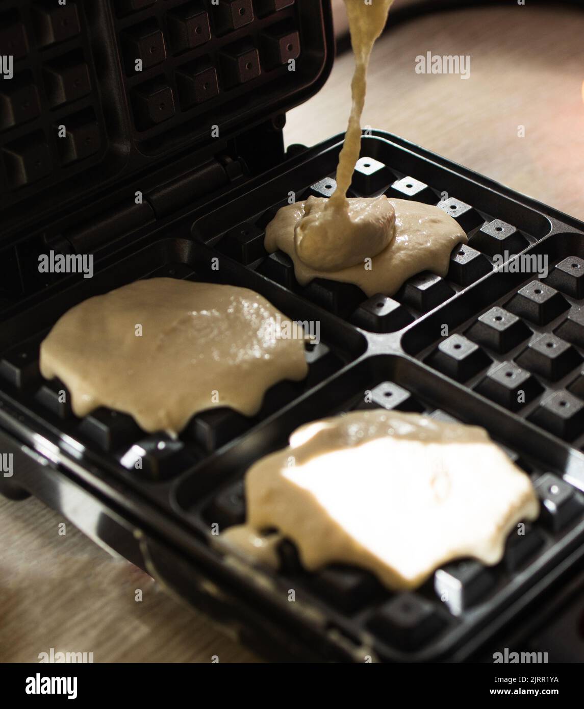 Cucina con waffle belgi in un ferro da stiro. Versare l'impasto. Foto Stock