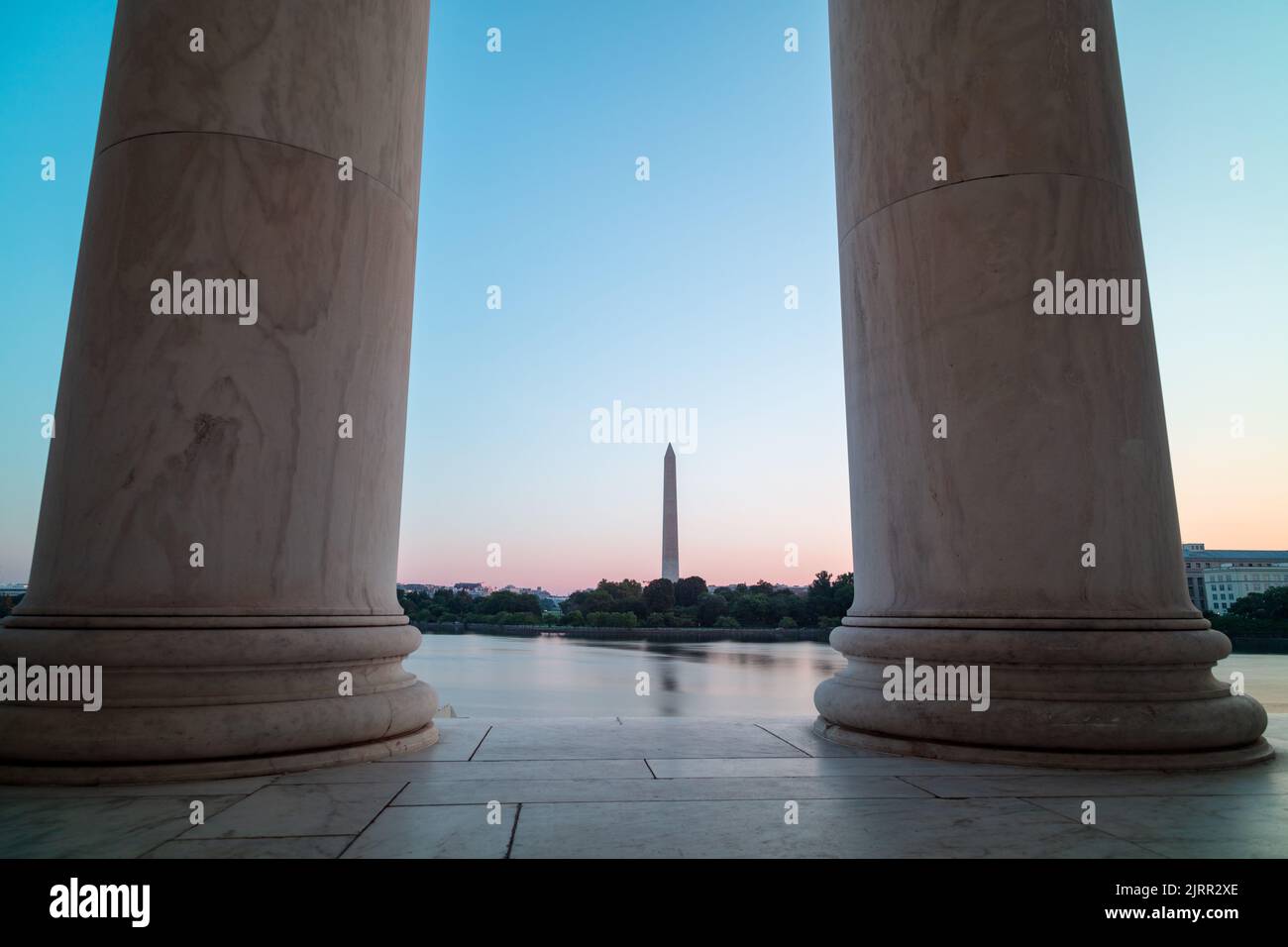 Il Washington Monument e la Casa Bianca sono visti dall'altra parte del Tidal Basin, incorniciato da due colonne nel Jefferson Memorial. Alba durante l'estate. Foto Stock