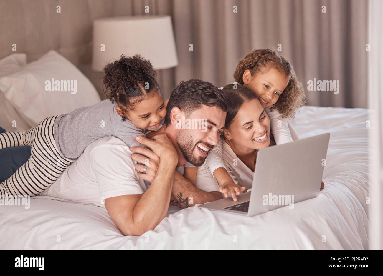 Buona visione dei film in streaming sul computer portatile in camera da letto per un intrattenimento online e un relax durante la notte a casa. Sorridi, madre e padre con le ragazze Foto Stock