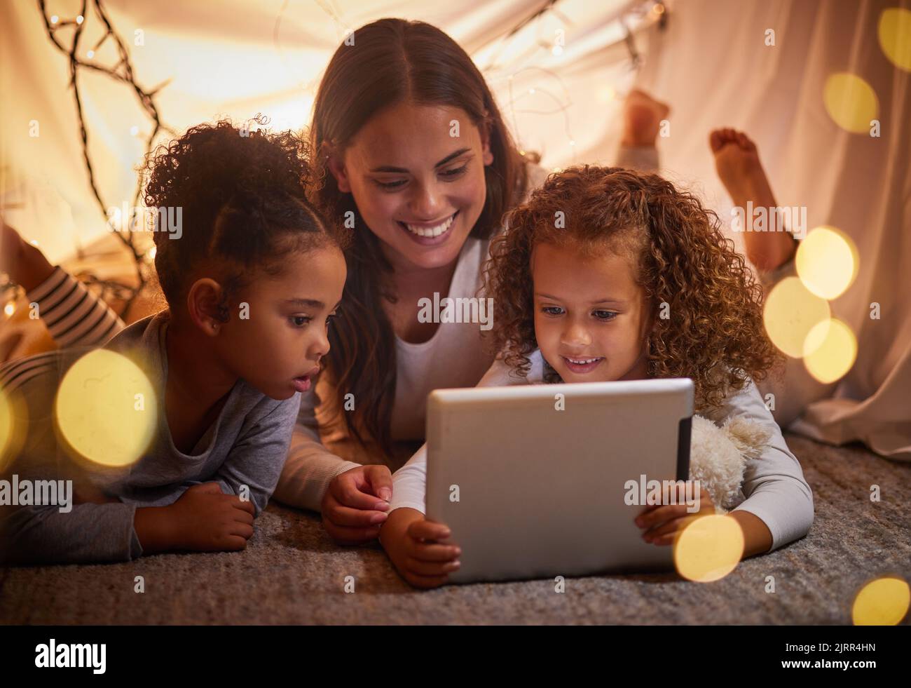 Tenda a casa madre e bambini sul tablet guardano film o film di intrattenimento per bambini online la sera a casa. Sorridere felice mamma o donna e ragazza giovane Foto Stock