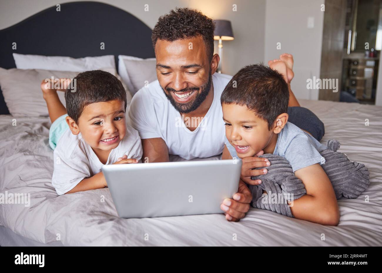 Felice, padre e bambini che guardano spettacoli di intrattenimento su un tablet digitale in camera da letto a casa. Tecnologia, uomo e bambini rilassarsi sul letto insieme a. Foto Stock