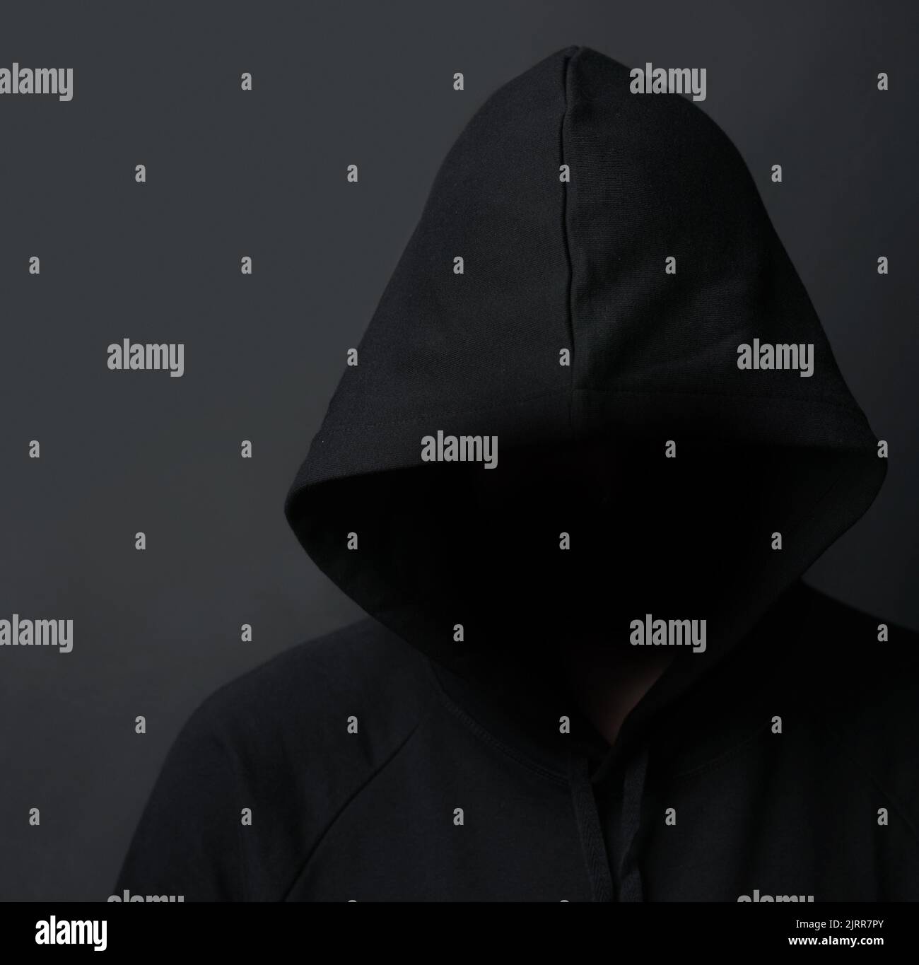 Pericolo in agguato al buio. Un uomo con cappuccio non identificabile che si posa su uno sfondo scuro. Foto Stock