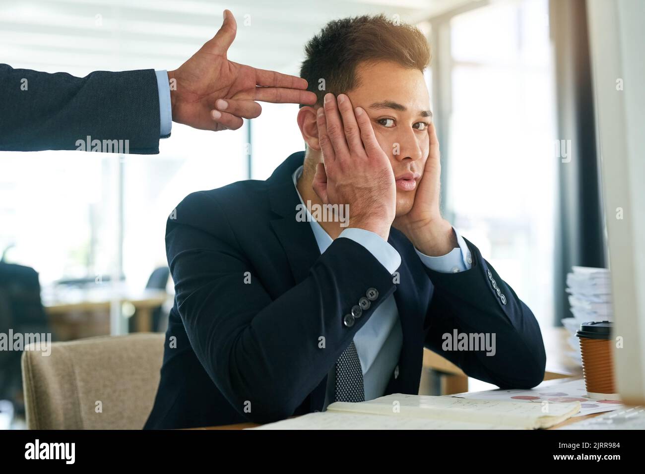 Si prova a lavorare in questo modo. Ritratto di un uomo d'affari che lavora mentre il suo capo si aggrae con una pistola alla testa. Foto Stock