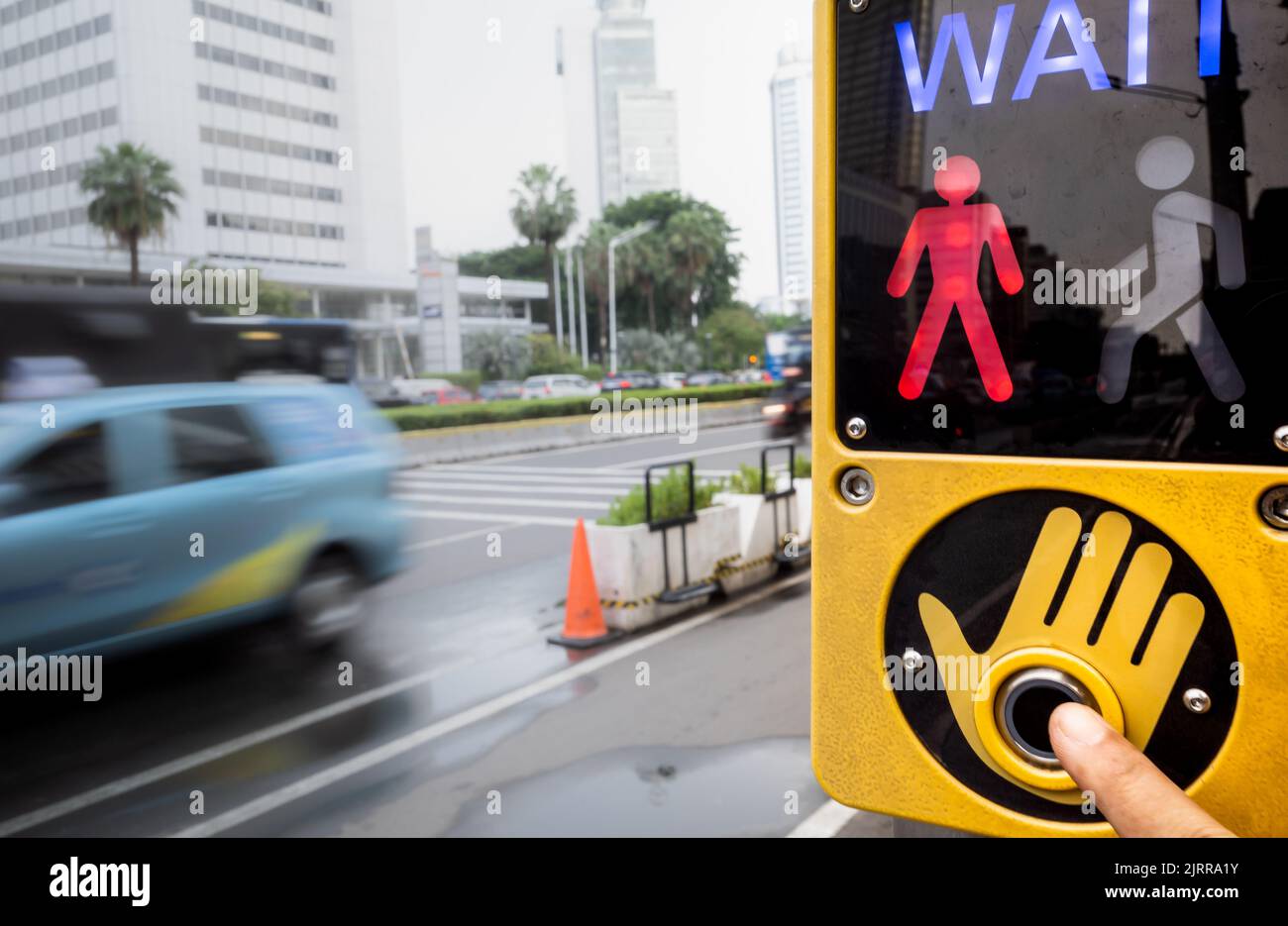 Persona toccare manualmente il pulsante del segnale a croce situato in una strada trafficata della città Foto Stock