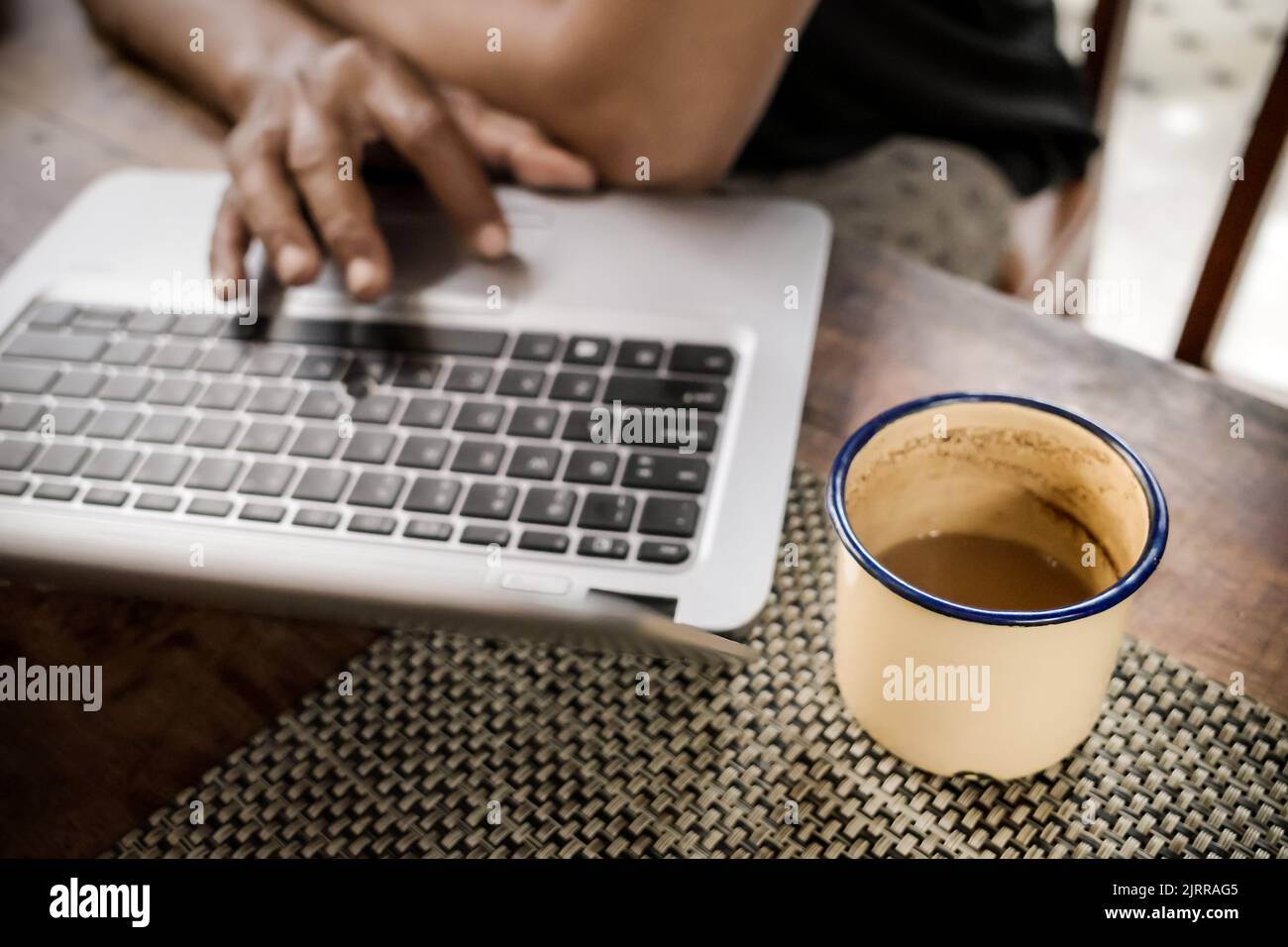 Un uomo che naviga su Internet utilizzando un notebook a casa accompagnato da un bicchiere di caffè Foto Stock