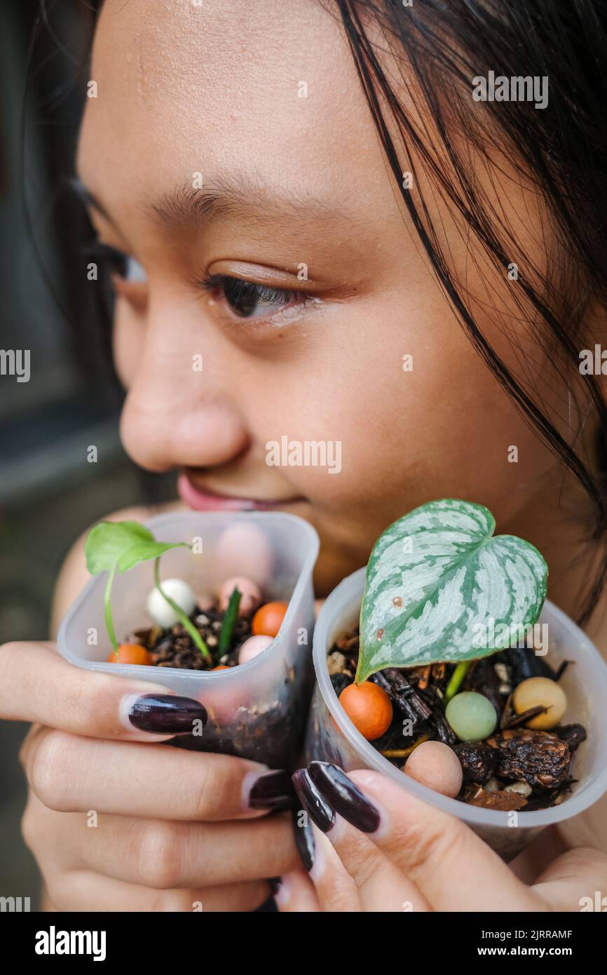Primo piano di ragazza asiatica teen che tiene piccole piante tropicali Foto Stock