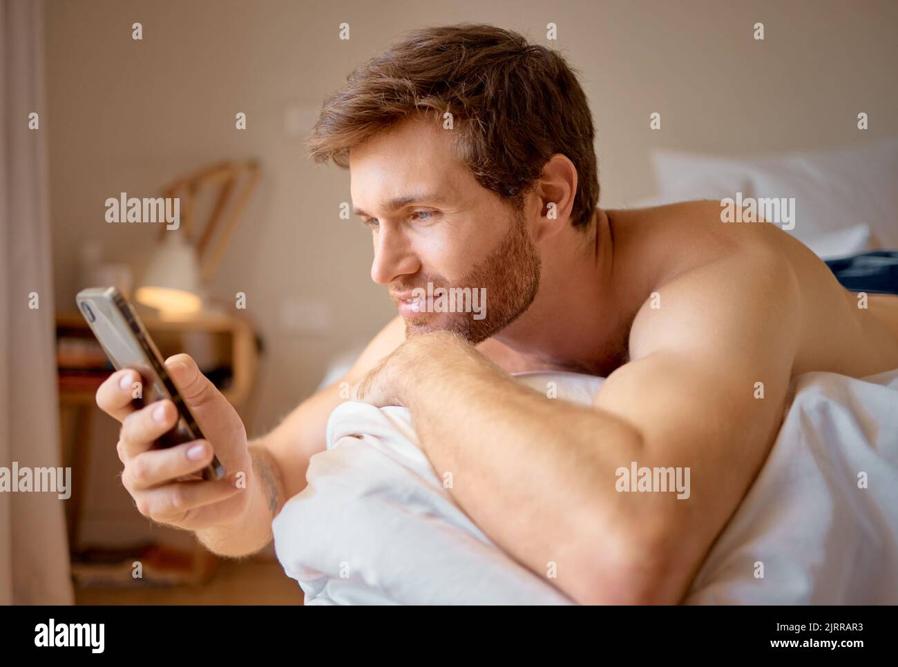 Telefono web dating app ricerca, internet streaming o SMS di un uomo attraente in una camera da letto letto. Digitale, online e social media su un dispositivo mobile 5g Foto Stock
