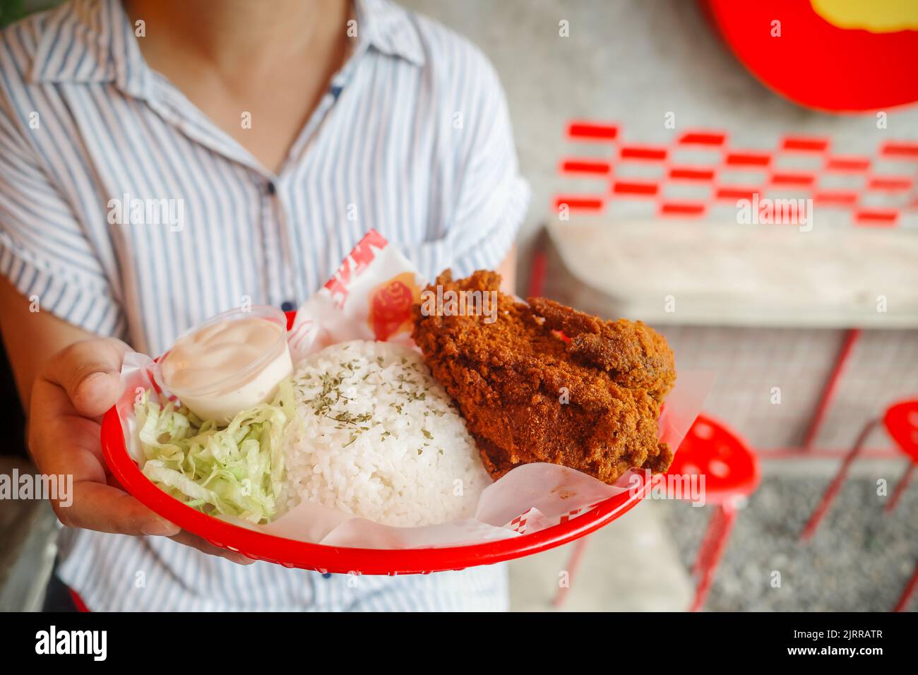 Donna asiatica che tiene un piatto di un delizioso pranzo in un ristorante fast food. Menu asiatico di pollo fritto piccante con riso. Foto Stock
