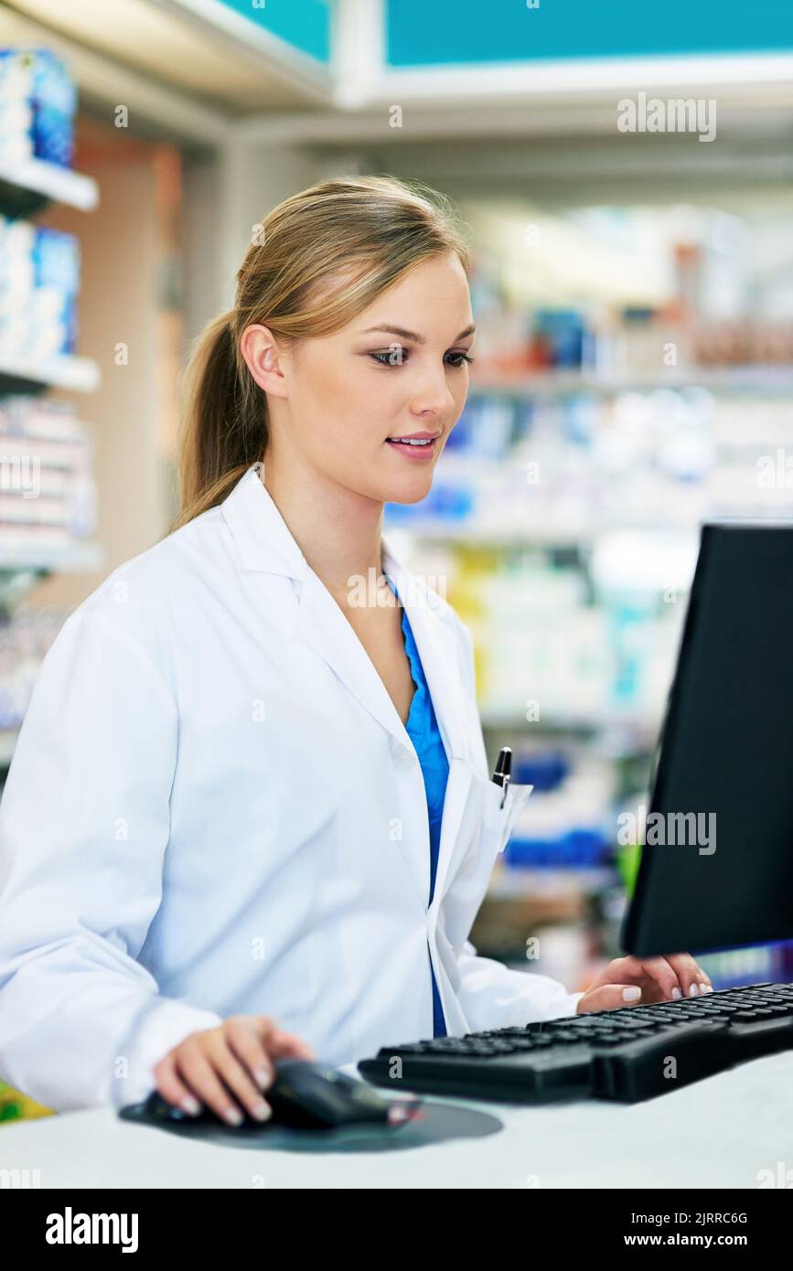 Tenere d'occhio i dati dei clienti. Un giovane farmacista che usa un computer al banco cassa. Foto Stock