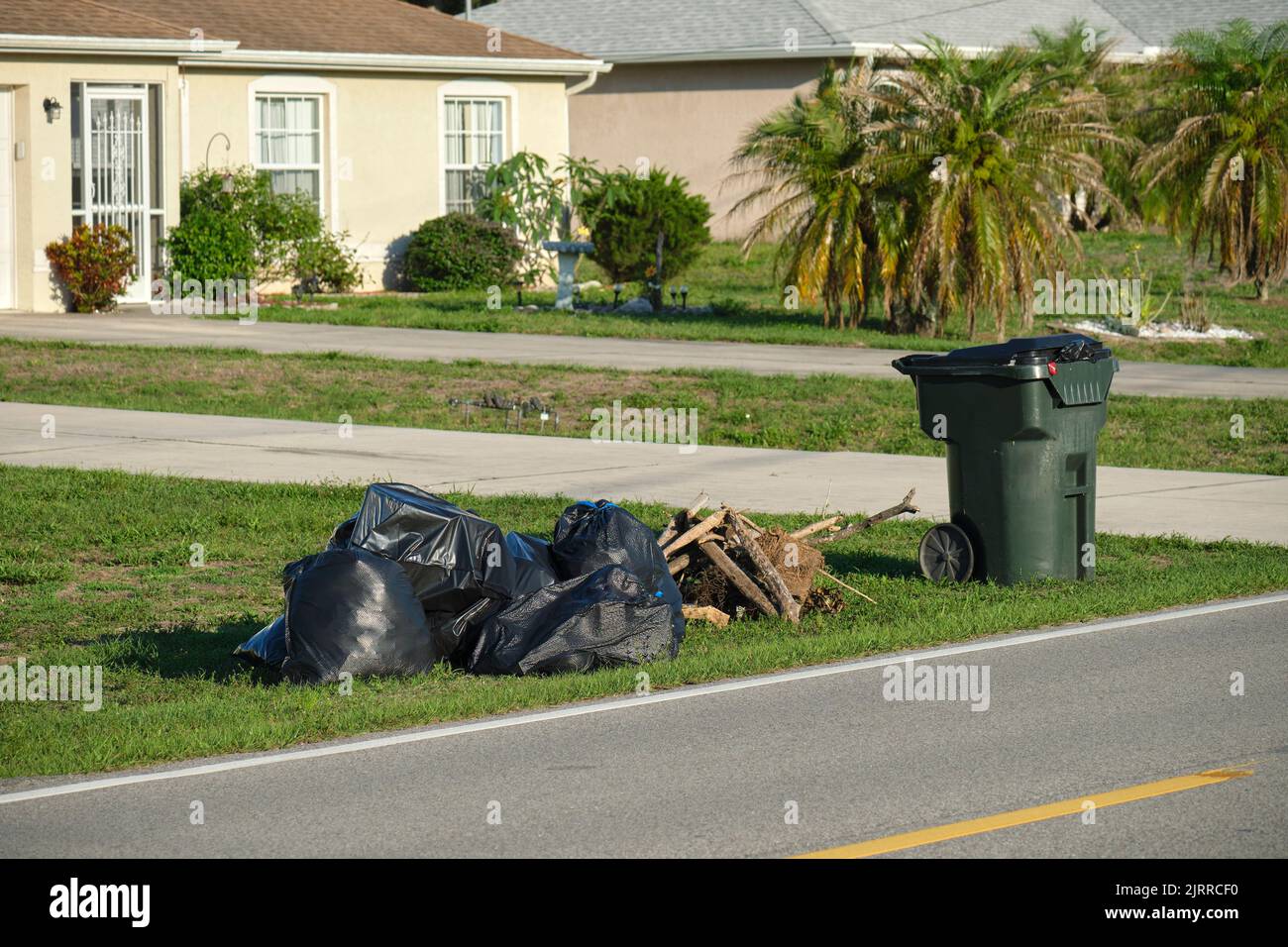 Mucchio di sacchi di rifiuti neri e bidone di plastica all'aperto sul lato rurale della strada. Problemi di gestione dei rifiuti Foto Stock