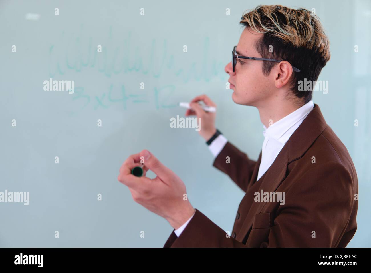Un professore universitario che disegna nel mezzo di una classe sulla lavagna. Elegante uomo in tuta che dà una scrittura di classe nella lavagna bianca. Foto di alta qualità Foto Stock