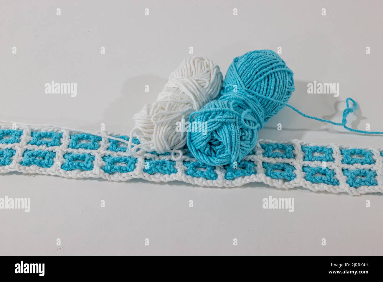 Tessuto intrecciato a crochet nei colori bianco e blu accanto a due palle di cotone contro superficie e sfondo bianco, disegno a forma quadrata e in l Foto Stock