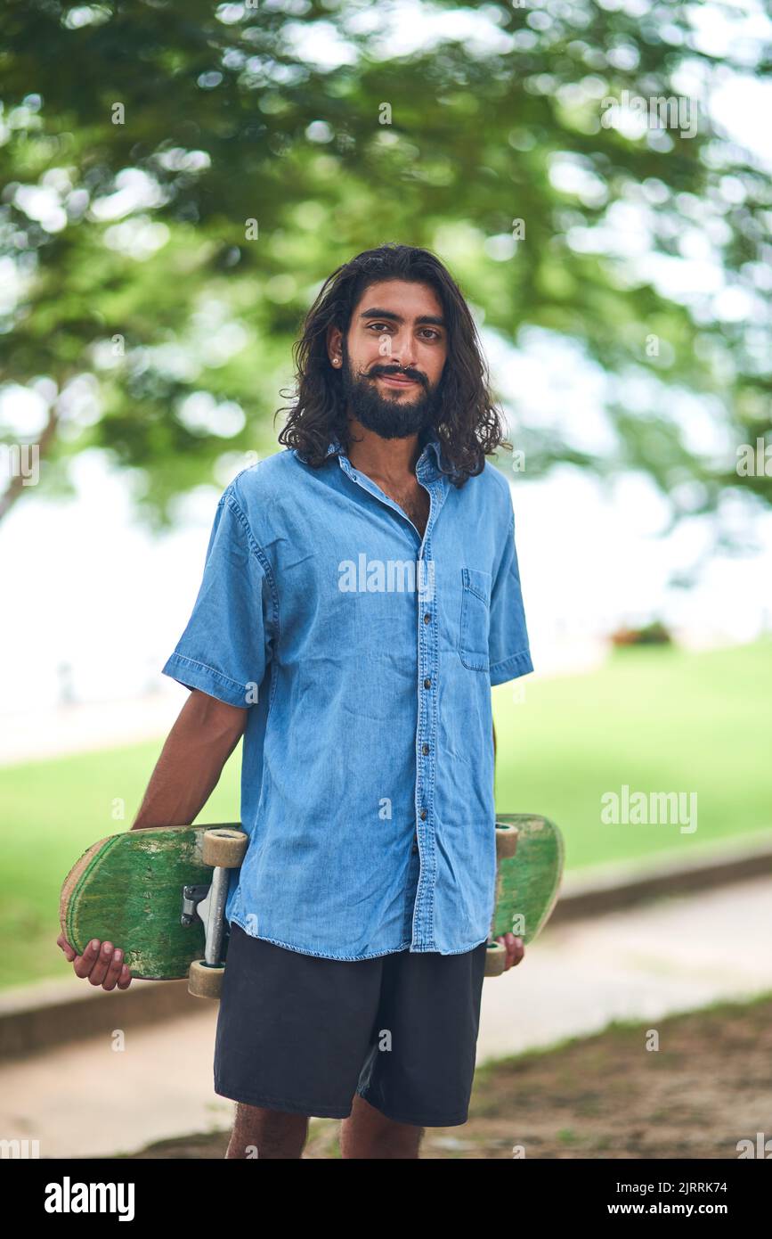 Pattinare è vita. Ritratto di un giovane sorridente che porta uno skateboard in piedi fuori in una giornata di sole. Foto Stock