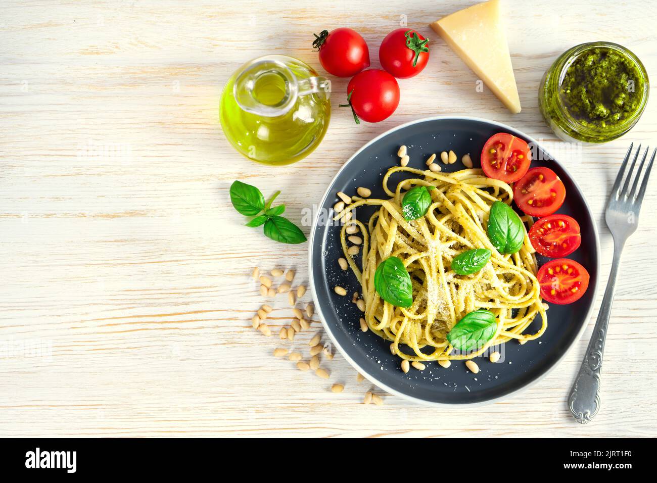 Pasta tradizionale italiana con verdure fresche, parmigiano, foglie di basilico, pinoli e salsa al pesto in piatto nero su fondo di legno bianco. T Foto Stock
