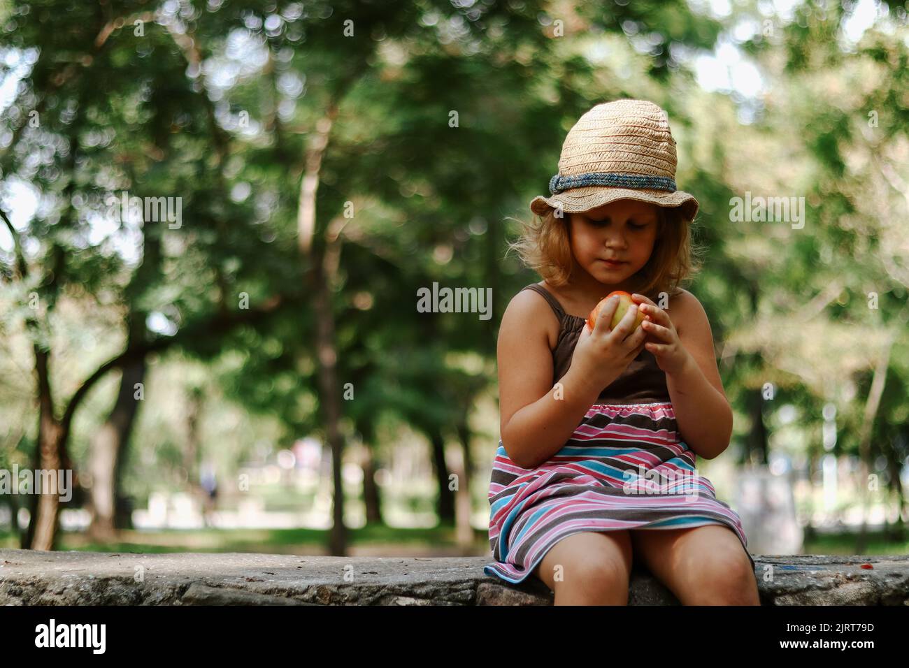 Ritratto di un bambino con una mela in mano. Il bambino di 5 anni mangia una mela. Ragazza in un cappello di paglia. Foto Stock