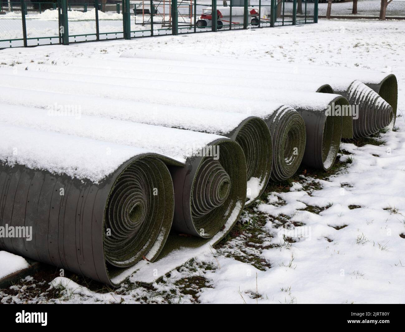 Rotoli di erba finta ricoperta di neve stanno aspettando in tempo. Erba sintetica per campi sportivi e stadi all'aperto Foto Stock