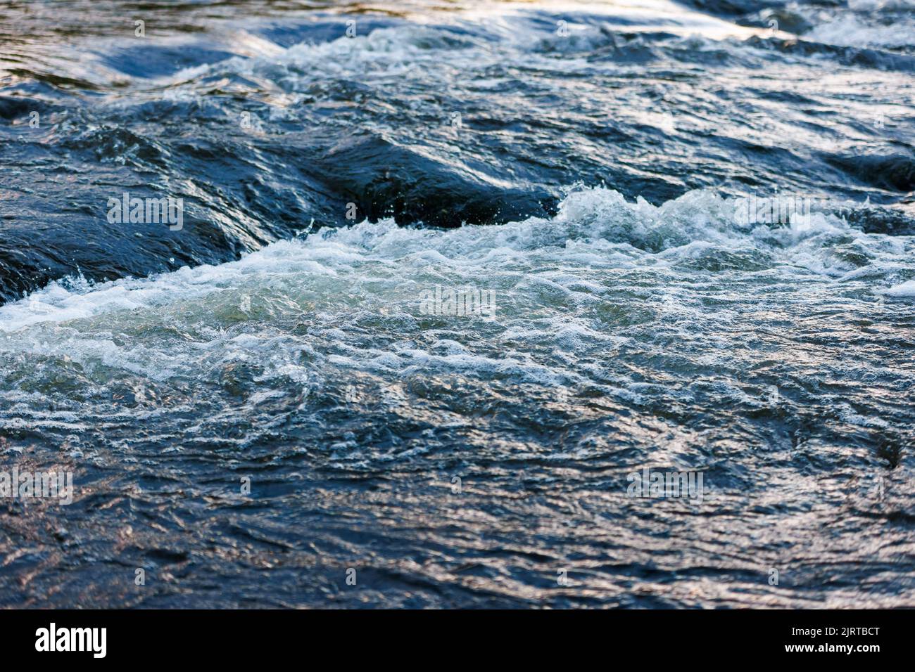 acqua fluente di un fiume estivo con una piccola e rapida cascata alla luce della sera Foto Stock