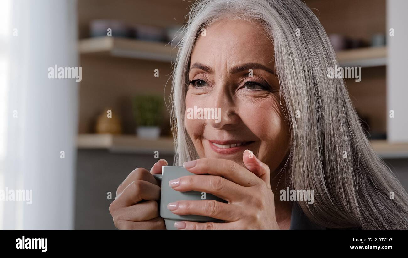 Sognante ispirato vecchia bionda grigio-capelli donna nonna nonna nonna maturo anziana pensionato donna di mezza età seduta in cucina bere caffè tè bevanda calda Foto Stock