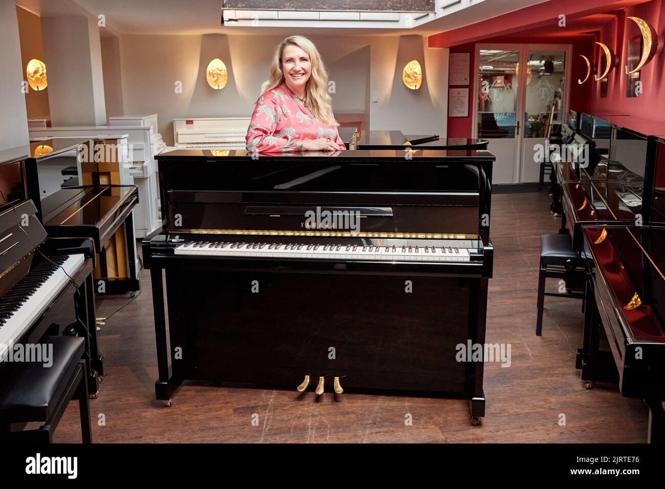 25 agosto 2022, Amburgo: Yvonne Trübger, proprietario, si trova dietro uno dei 15 pianoforti da donare per celebrare il 150th° anniversario della Pianohaus Trübger. La piano house è una delle ultime case pianistiche che non rappresenta un solo marchio. (A dpa 'Pianohaus Trübger dà via 15 pianoforti per 150th anniversario') Foto: Georg Wendt/dpa Foto Stock