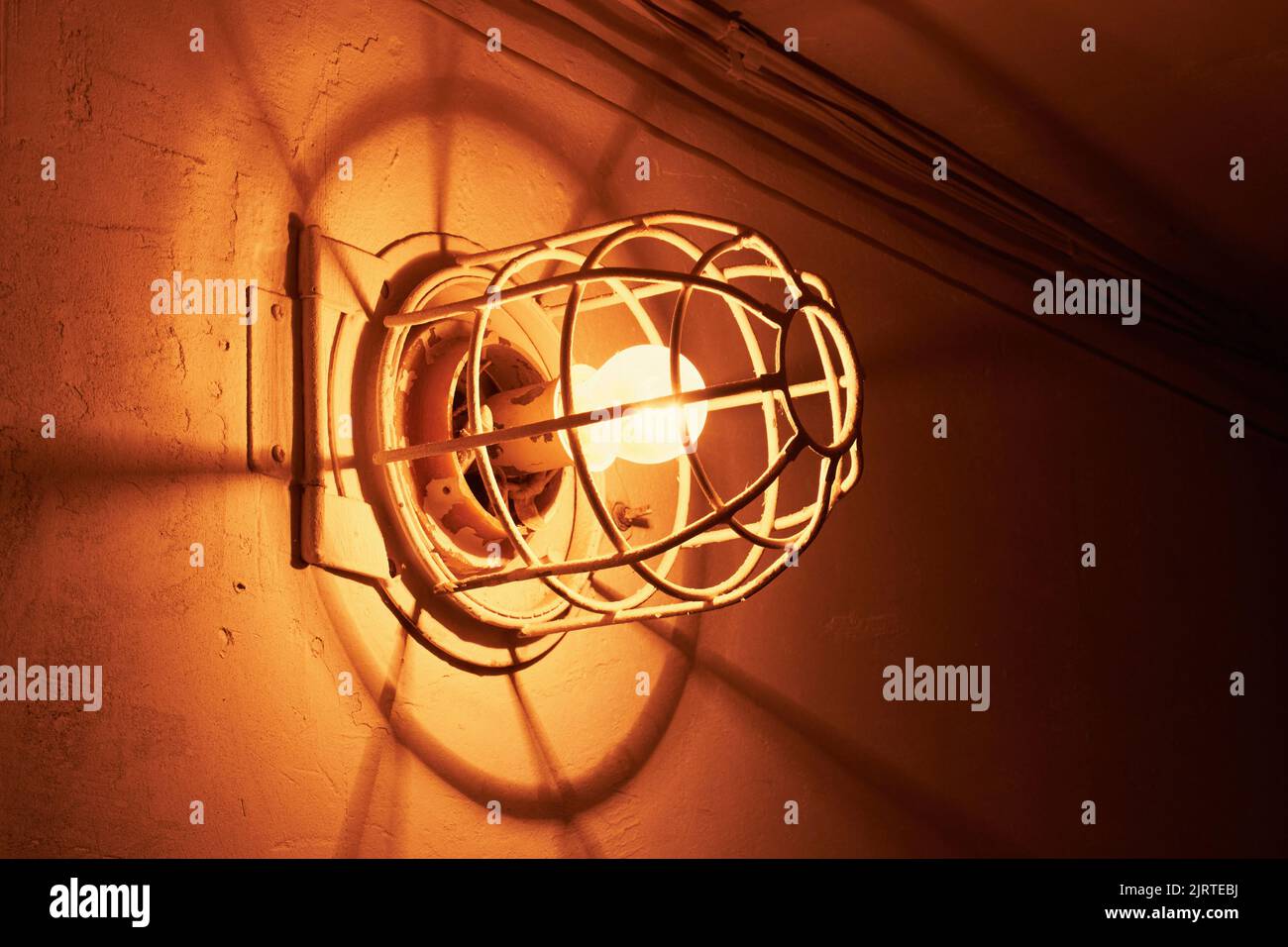 Lampada a incandescenza luminosa. Vecchia lampadina elettrica con una griglia metallica sulla parete Foto Stock