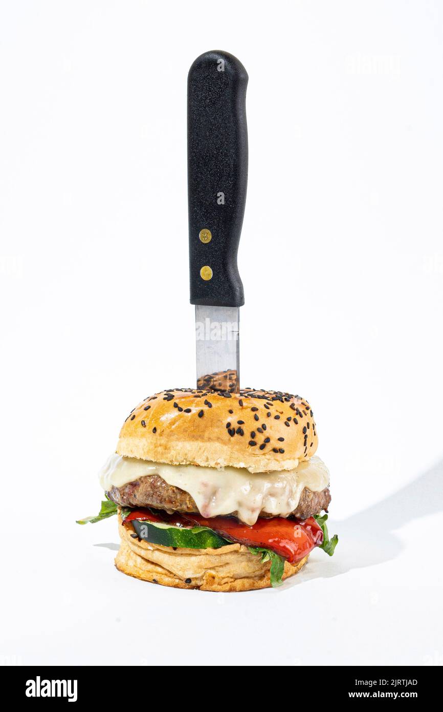 Un colpo verticale di un cheeseburger con un coltello su uno sfondo bianco Foto Stock
