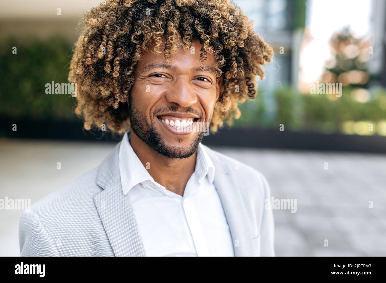 Foto ravvicinata di un uomo brasiliano o ispanico, un dirigente di successo, sicuro e carismatico, dai capelli ricci, che guarda la fotocamera, sorridendo amichevole Foto Stock