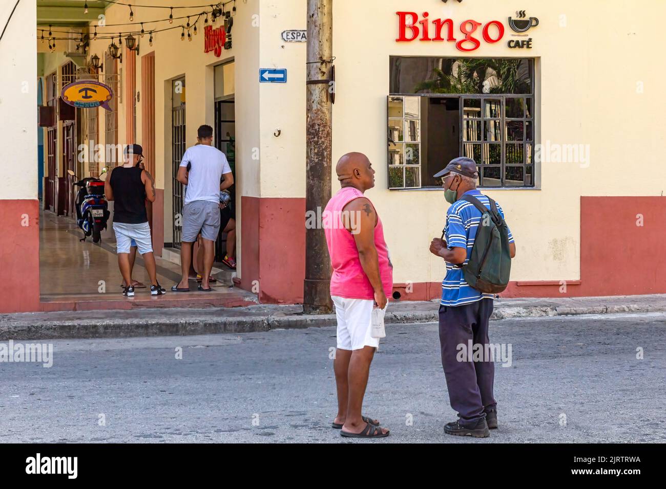 Due cubani afro-caraibici parlano in una strada cittadina. Sullo sfondo, una piccola impresa nome Bingo Cafe Foto Stock