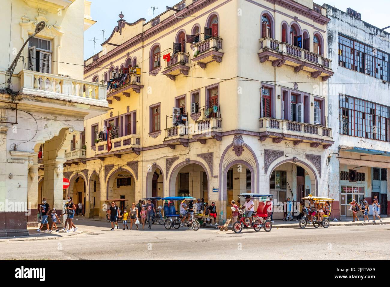 Un gruppo di lavoratori autonomi guida pedicabs o bicitassi in un angolo della città. Un edificio di vecchio stile con archi si trova nell'area. Foto Stock