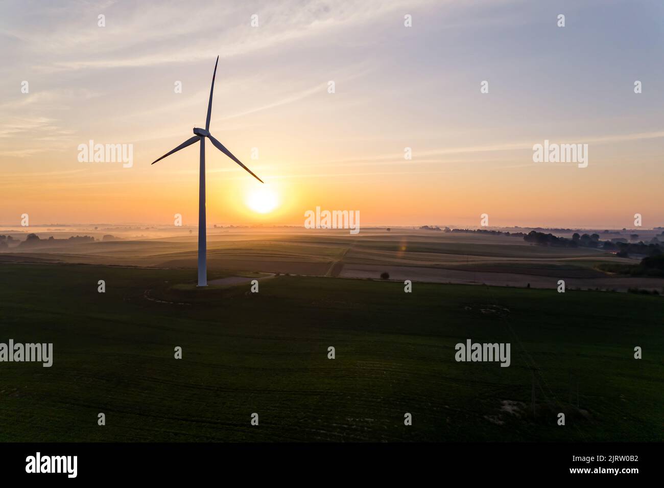 Silhouette di turbina eolica in piedi in verde campo agricolo con il sole luminoso che sorge sullo sfondo. Fonti di energia ecologamente amichevoli. Scatto orizzontale. Foto di alta qualità Foto Stock