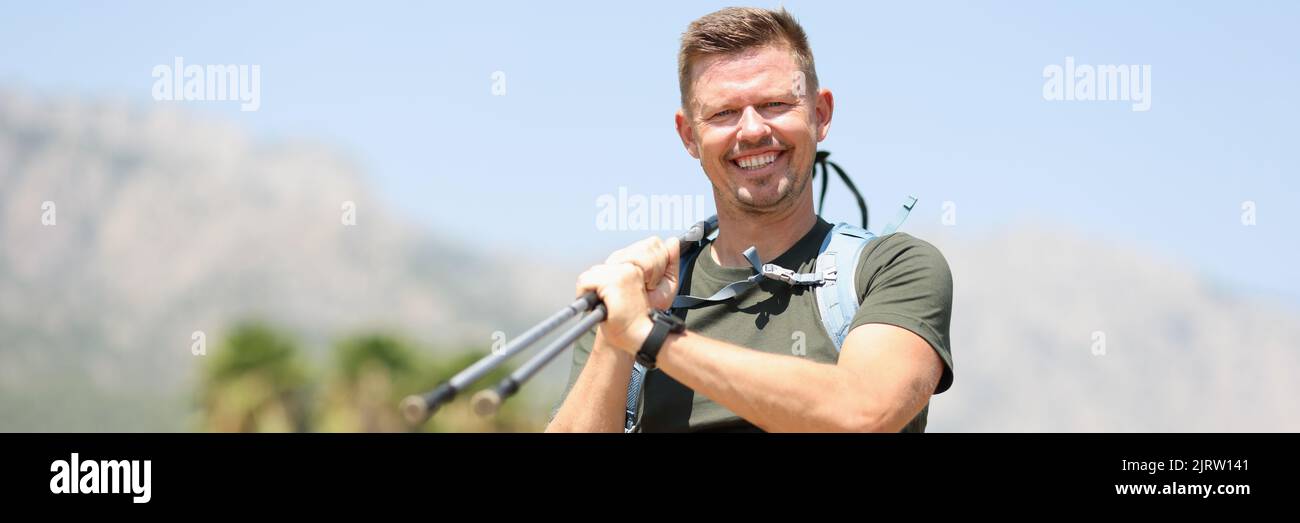 Giovane uomo sorridente in montagna con bastoni finlandesi Foto Stock