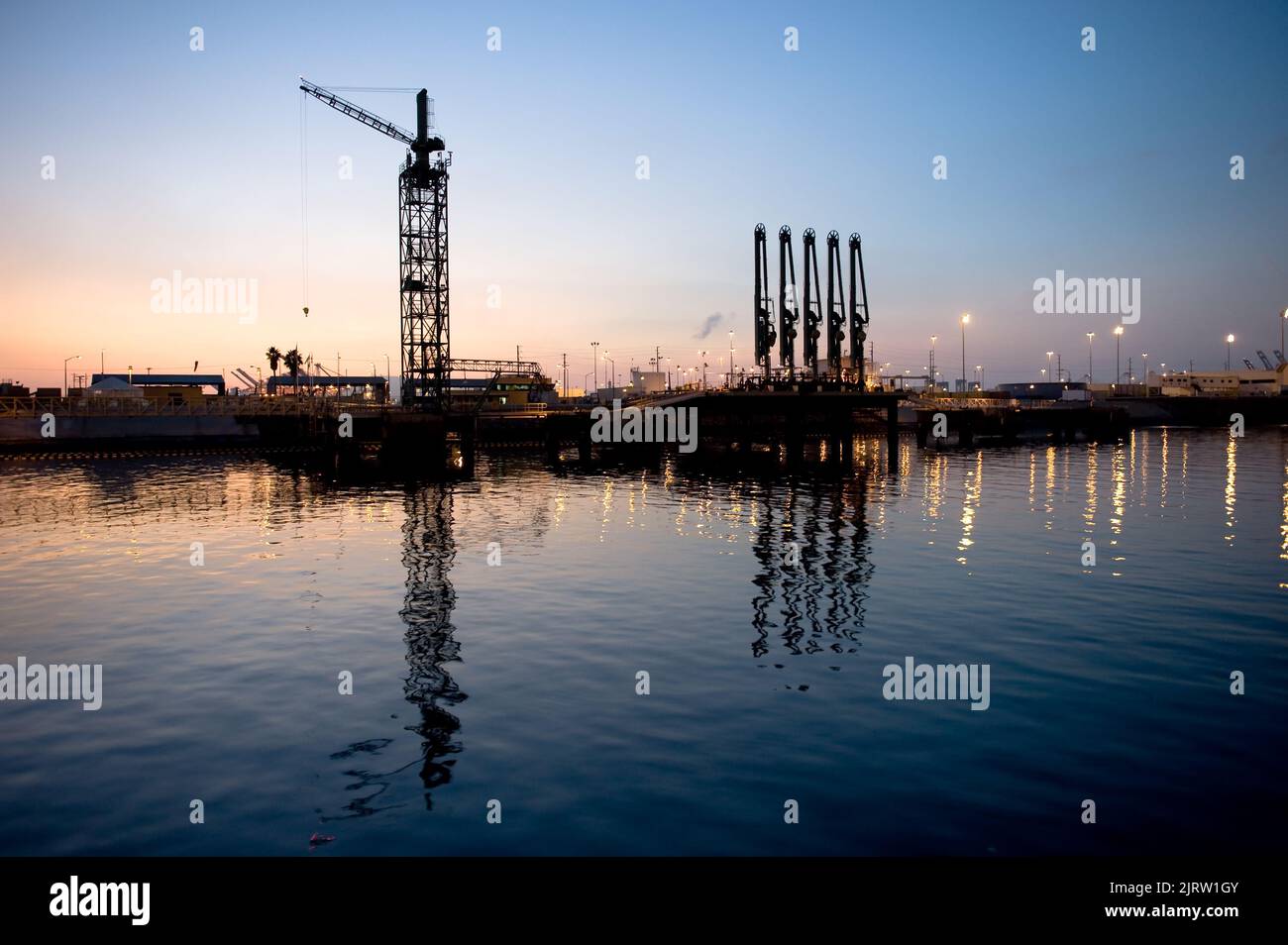 Una petroliera il carico e lo scarico di dock con paranco gru e pompe olio in un porto industriale durante il tramonto. Foto Stock