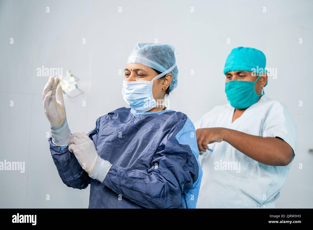 infermiera che aiuta la donna chirurgo a indossare abito operatorio per la chirurgia - concetto di occupazione professionale, carriera e personale di supporto. Foto Stock