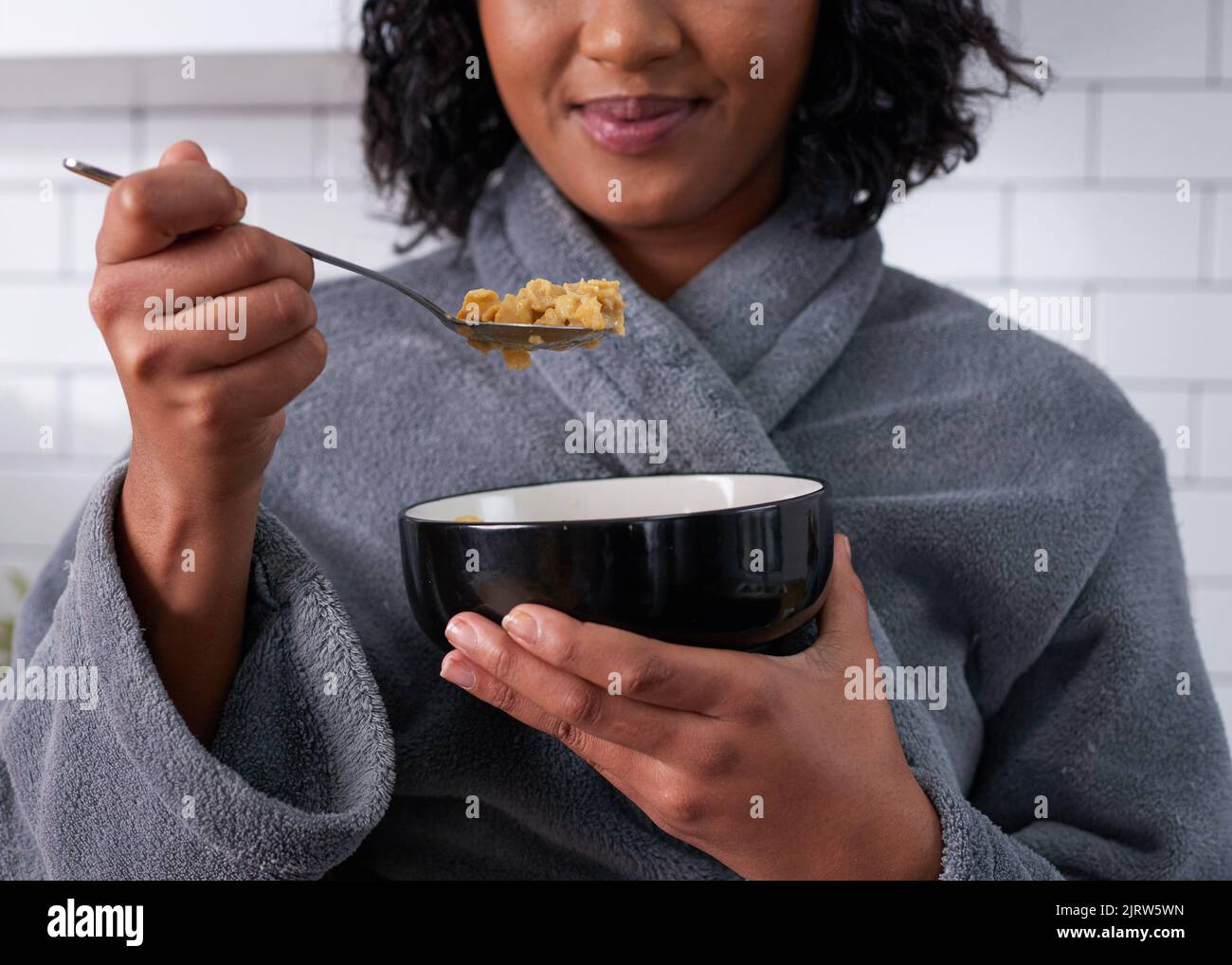 Un primo piano di cornflakes su un cucchiaio, mentre la donna mangia la colazione in abito Foto Stock