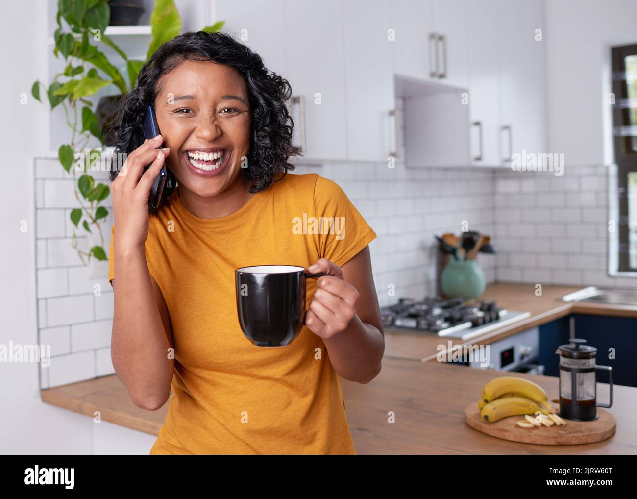 Una giovane donna multietnica ride mentre è al telefono in cucina Foto Stock