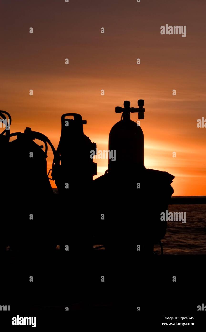 I carri armati scuba si siedono su una barca durante un bellissimo tramonto in mare. Foto Stock